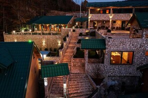 A multi-story building with stone walls and green roofs, featuring outdoor seating areas and a visible interior space. - Garni Eco Hotel Elite Kolasin (Kolašin)