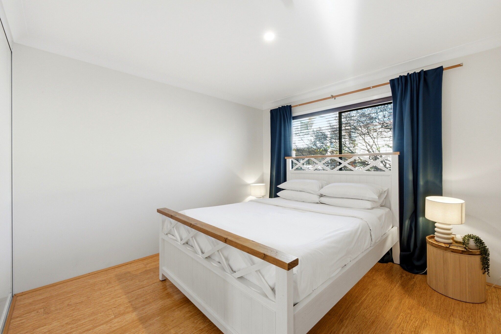 A bedroom with a bed, a nightstand, a window with curtains, and a wooden floor.