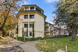Ein mehrstöckiges Wohngebäude mit flachem Dach, einem Balkon im zweiten Stock und einem gepflegten Garten mit einem Weg.
