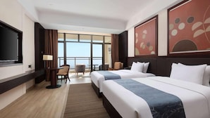 Quarto de hotel com duas camas, uma escrivaninha, uma cadeira, televisão e janelas amplas com vista.