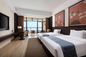 Habitación de hotel con dos camas, un escritorio, una silla, un televisor y ventanas amplias con vistas.