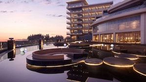 Um hotel moderno com piscina infinita no terraço, várias varandas e fachada bem iluminada.