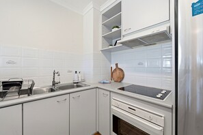 A kitchen with white cabinets, a stainless steel refrigerator, a black stovetop, and a dish rack. - Spacious 2-Bedroom Retreat with Golf Course Views (Narrabundah)