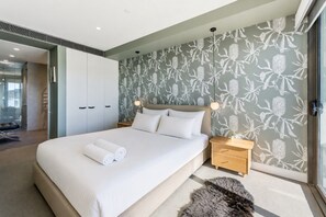 A modern bedroom with a large bed, a nightstand, a wardrobe, and a bathroom visible in the background. - Waterfront 1-Bed Apartment in Kingston (Kingston)