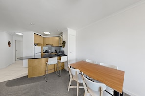 A modern kitchen with a central island, white chairs, and a wooden dining table. - Top Floor Braddon | Sunset Views to Black Mountain (Braddon)