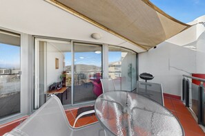 Ein Balkon mit Glastür, einem Tisch und einem Grill.