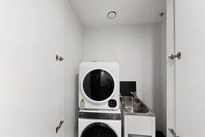 A compact laundry room with a front-loading washer and dryer, a small sink, and a door with a handle. - Executive 2-Bed Apartment Near Kingston Hub (Kingston)