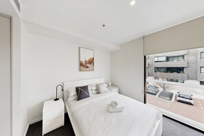 A modern hotel room with a large bed, a bedside table, a nightstand, a framed picture on the wall, and a view of the outside. - Executive 2-Bed Apartment Near Kingston Hub (Kingston)
