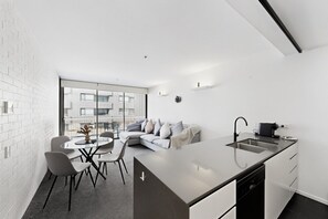 A modern kitchen with a large island, a dining area with chairs and a table, and a living space with a sofa and cushions. - Executive 2-Bed Apartment Near Kingston Hub (Kingston)