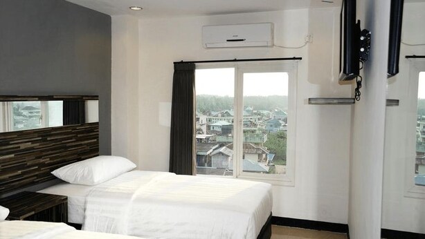 A hotel room with two beds, a large window with a view, and a mounted TV. - Galaxy Hotel (Tarakan)