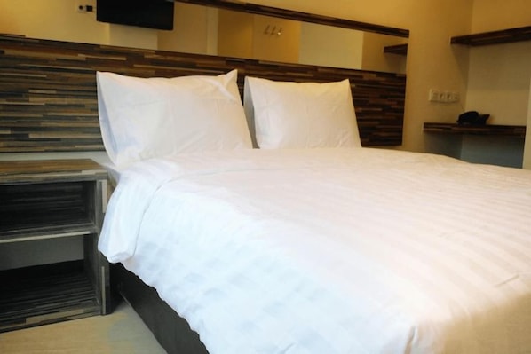 A hotel room with a large bed, a bedside table, and a flat-screen TV mounted on the wall.
