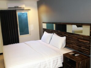 A hotel room with a large bed, a wooden headboard, a nightstand, and a window with curtains. - Galaxy Hotel (Tarakan)