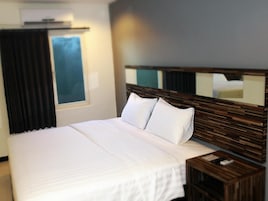 A hotel room with a large bed, a wooden headboard, a nightstand, and a window with curtains.