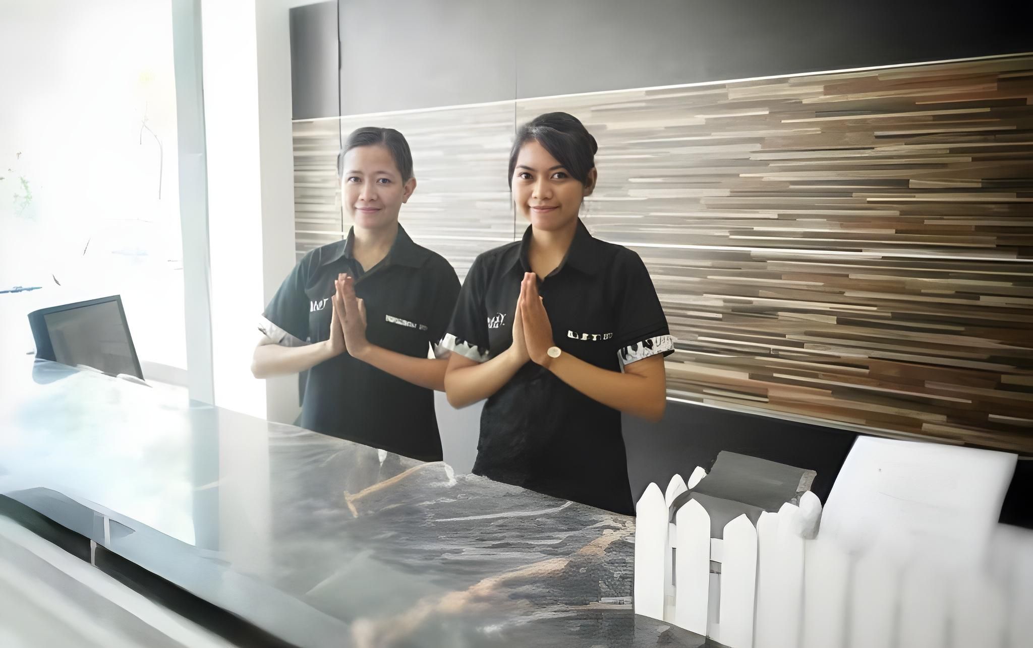 Two individuals standing at a reception desk with a modern design, including a patterned wall and a white fence model.