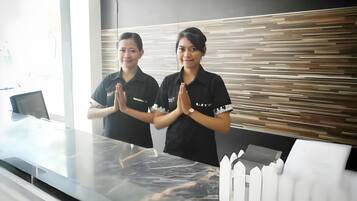 Two individuals standing at a reception desk with a modern design, including a patterned wall and a white fence model.