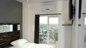 A hotel room with a bed, a nightstand, a window with curtains, an air conditioning unit, and a view of buildings outside. - Galaxy Hotel (Tarakan)