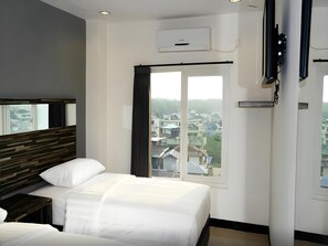 Et hotelværelse med seng, et natbord, et vindue med gardiner, en aircondition og udsigt til bygninger.