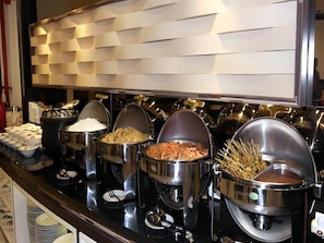 A buffet with various food items in metal containers, including rice, fried chicken, and vegetables.