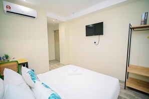 Una habitación de hotel con cama, un televisor de pantalla plana en la pared, una mesita con una planta y una estantería con libros.