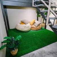 Un rincón pequeño y acogedor con suelo de césped artificial verde, rodeado de una escalera y plantas en macetas.