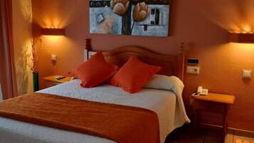 Una habitación de hotel con una cama, almohadas rojas, un cuadro en la pared y dos lámparas de noche.