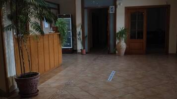 Un área de recepción con mostrador, plantas en macetas y piso de baldosas.