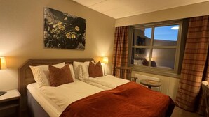 Ein Hotelzimmer mit Bett, Nachttischen, einem Fenster mit Vorhängen und einem Bild an der Wand.