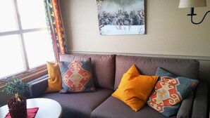Ein Wohnzimmer mit einer Couch, gemusterten Kissen, einem Gemälde, einer Lampe und einem Fenster mit Vorhängen.