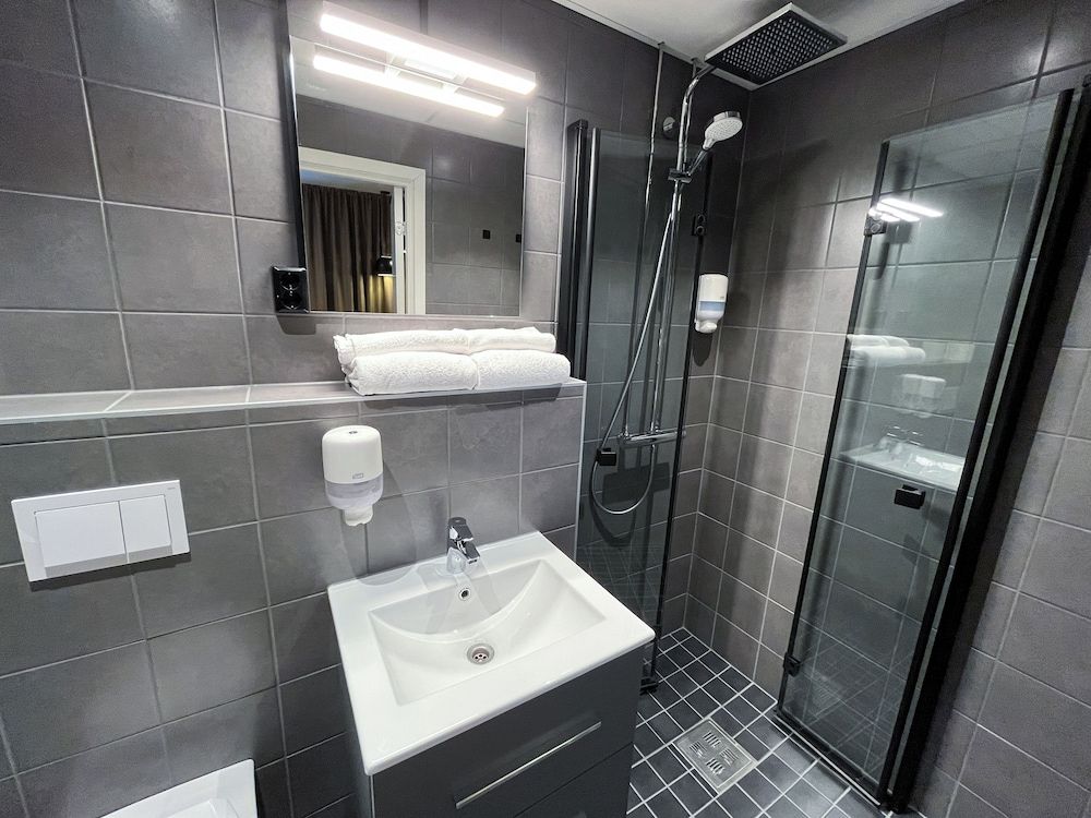 Un baño moderno con lavamanos, espejo, toallero y cabina de ducha de vidrio.