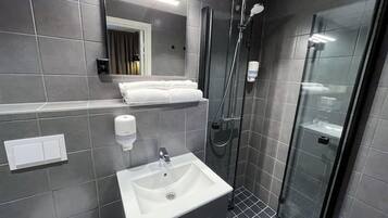 Un baño moderno con lavamanos, espejo, toallero y cabina de ducha de vidrio.