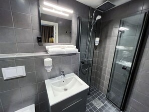 Un baño moderno con lavamanos, espejo, toallero y cabina de ducha de vidrio.