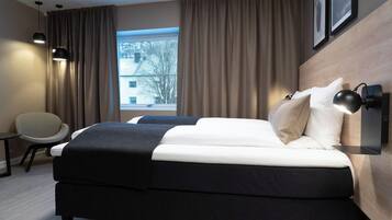 Una habitación de hotel moderna con cama, una silla, un escritorio y un ventanal con cortinas.
