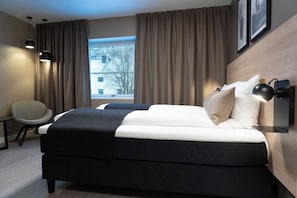 Una habitación de hotel moderna con cama, una silla, un escritorio y un ventanal con cortinas.