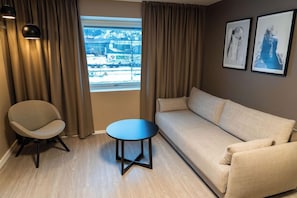 Una habitación con sofá, una silla, una mesita y una ventana con cortinas.