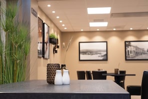 Habitación de hotel con una mesa de comedor, sillas, una planta y cuadros en la pared.