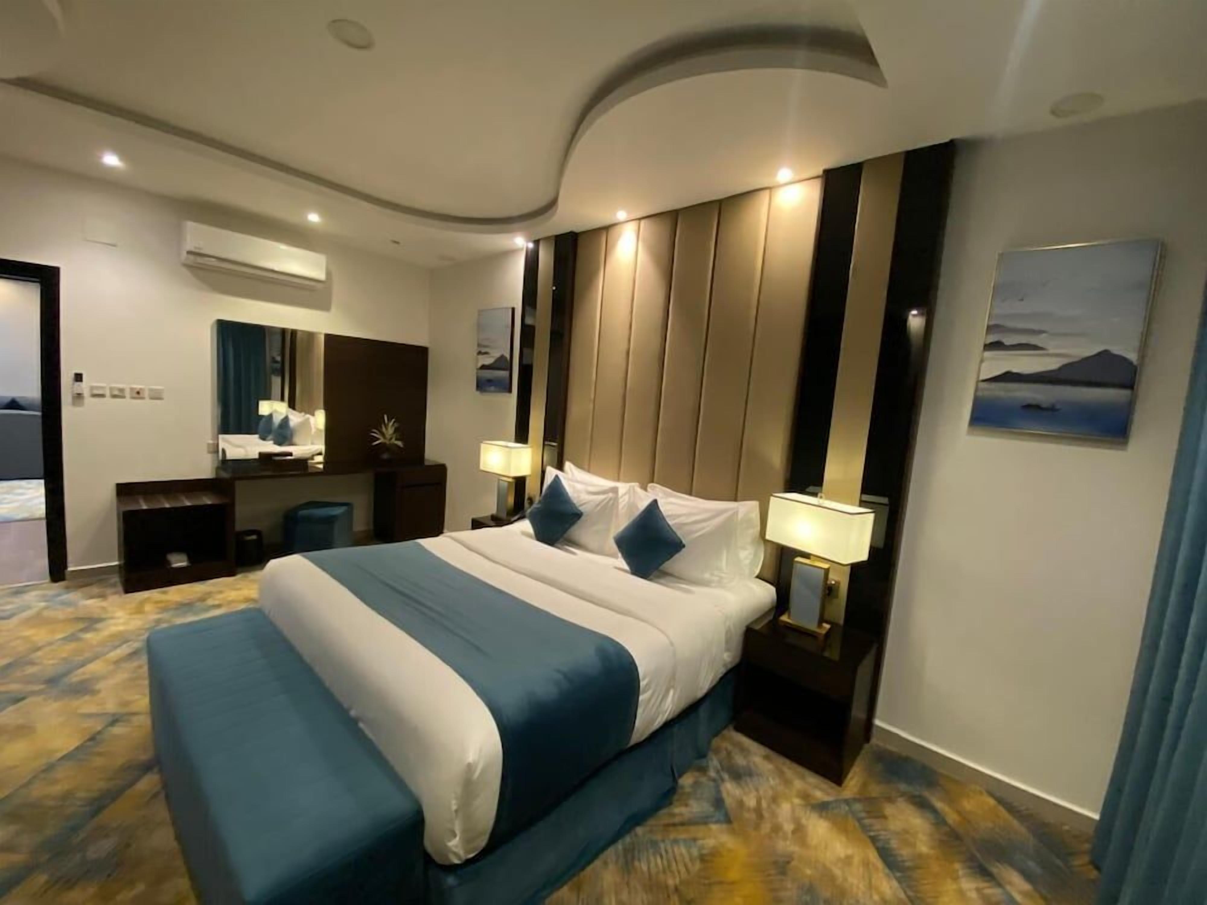 A hotel room with a large bed, bedside tables, a mirror, and a painting on the wall.