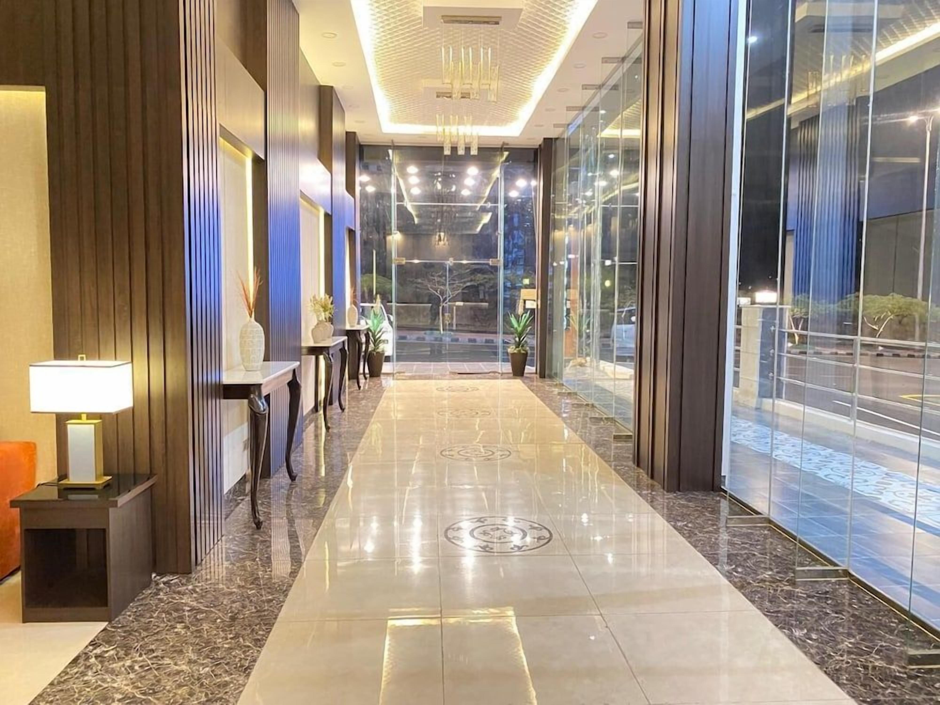A hotel lobby with a marble floor, a reception desk, and a view through large glass doors.