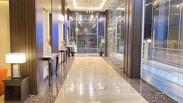 A hotel lobby with a marble floor, a reception desk, and a view through large glass doors.