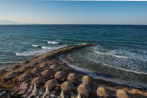 Una playa con sombrillas de paja, sillas de descanso, un rompeolas rocoso y el mar.