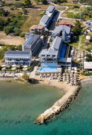 Un hotel frente al mar con varias construcciones, piscina y zona de playa.