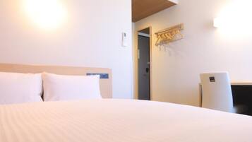 A hotel room with a bed, an air conditioning unit, a desk, and a coat rack.