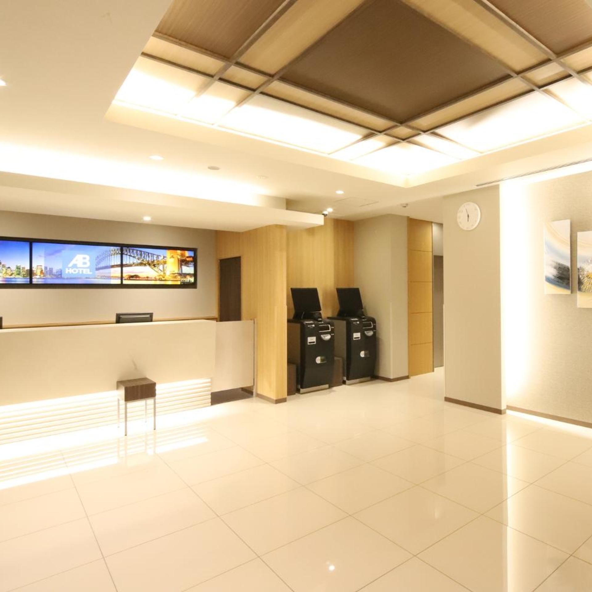 A hotel reception area with a digital screen displaying a cityscape, a reception desk, a clock, and a trash bin.