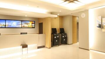 A hotel reception area with a digital screen displaying a cityscape, a reception desk, a clock, and a trash bin.