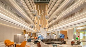 Een ruime lobby met een centraal zithoek, een moderne kroonluchter en een receptiebalie.