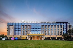 Un hôtel moderne doté d’une grande façade en verre, d’une entrée imposante et d’une pelouse bien entretenue.