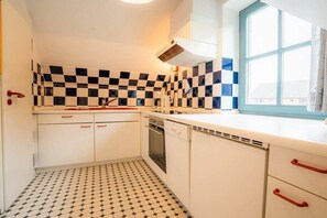 A compact kitchen with checkered tiles, white cabinets, and a window with blue trim. - OG in the Reimer house (ID 313) (St. Peter-Ording)