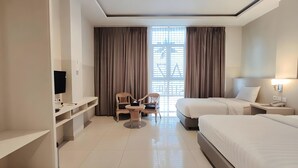 Habitación de hotel con televisión, escritorio, dos camas y ventana con cortinas.