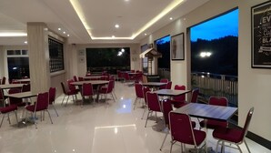 Un amplio comedor interior con varias mesas y sillas, un ventanal que ofrece vistas al exterior e iluminación empotrada en el techo.