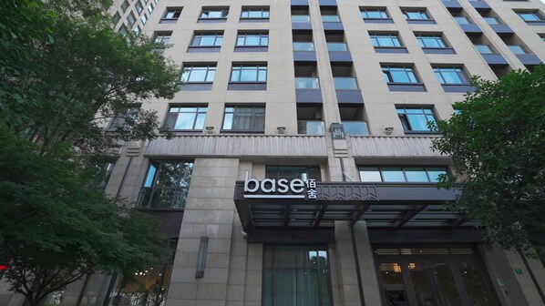 Un edificio de varios pisos con un llamativo letrero 'base' en la entrada, rodeado de árboles.