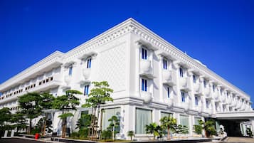 A white building with multiple windows and balconies, surrounded by greenery.